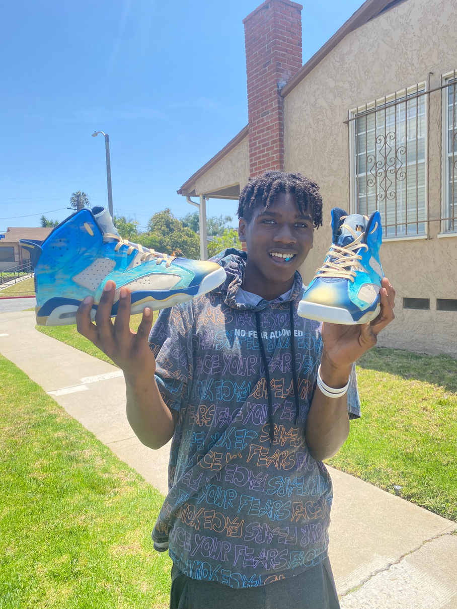 A young person holding up two custom-painted sneakers
