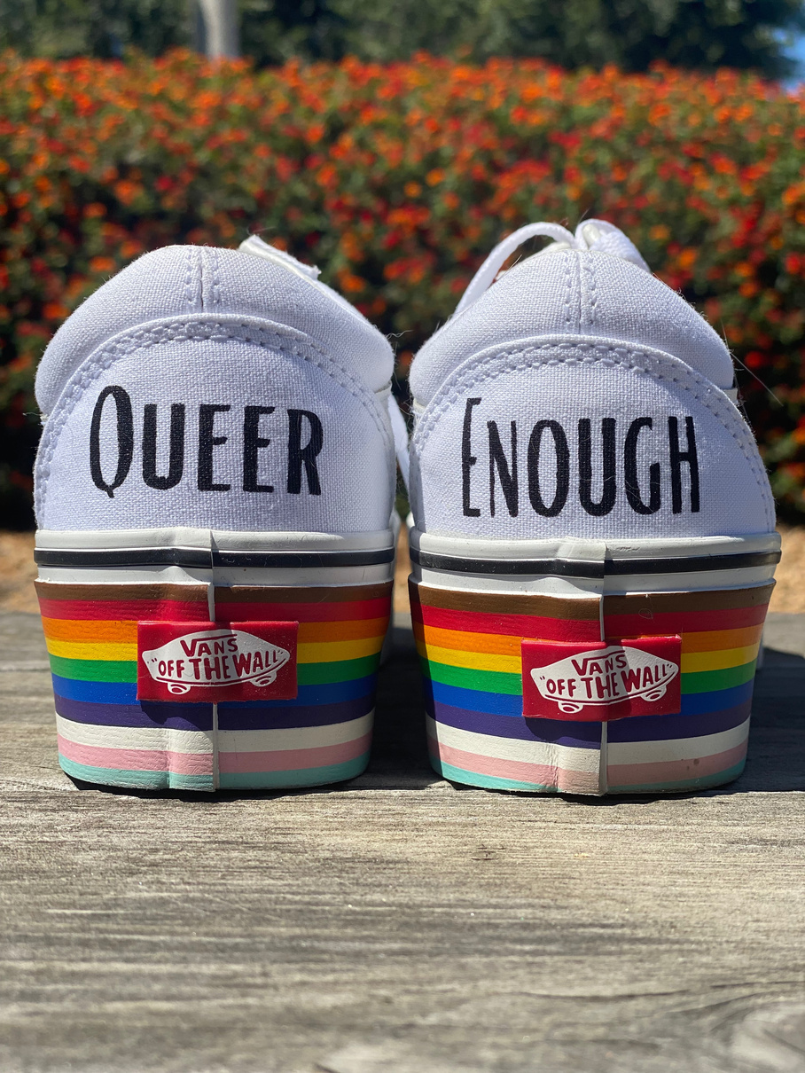 White Vans sneakers painted with the words QUEER and ENOUGH with rainbow soles